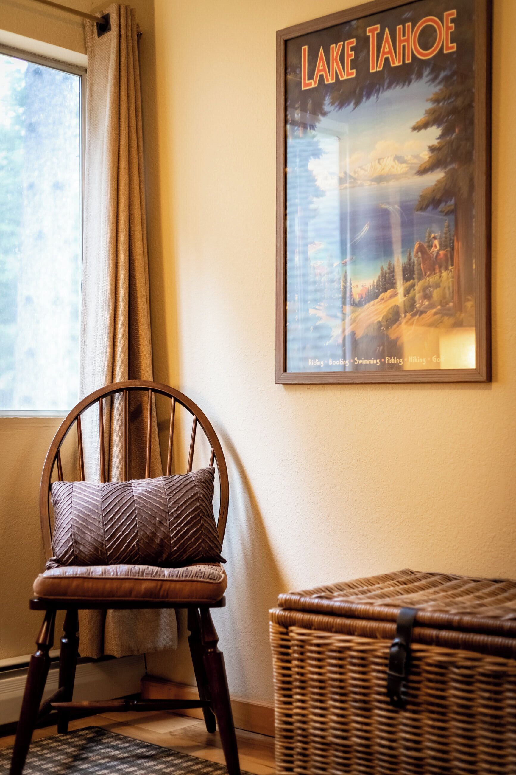 Uma cadeira com almofada estampada, uma cesta de vime e um quadro com imagem do Lago Tahoe na parede.