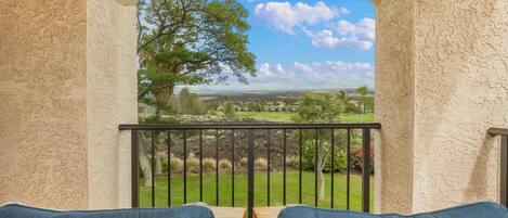 A balcony with wicker furniture and a view of a green landscape.