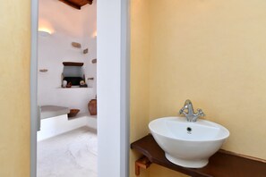 Casa de banho com lavatório branco sobre bancada de madeira, uma prateleira com objetos decorativos e uma parede branca com padrão texturizado.