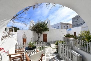 A courtyard with a white fence, a table with chairs, and a building with a bell tower. - Kastro Cozy Guesthouse (Paros)