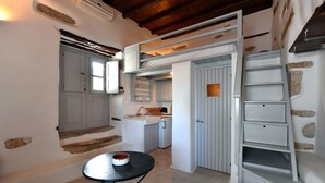 A compact kitchen with a sink, cabinets, and a small dining area with a table and chairs. - Kastro Cozy Guesthouse (Paros)