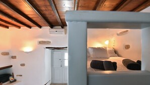 A cozy room with a bed, a nightstand, a lamp, and a stone wall. - Kastro Cozy Guesthouse (Paros)