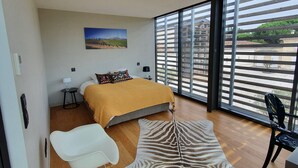 Un dormitorio moderno con una cama, un felpudo estampado con diseño de cebra, una silla blanca y vistas a través de grandes ventanales.