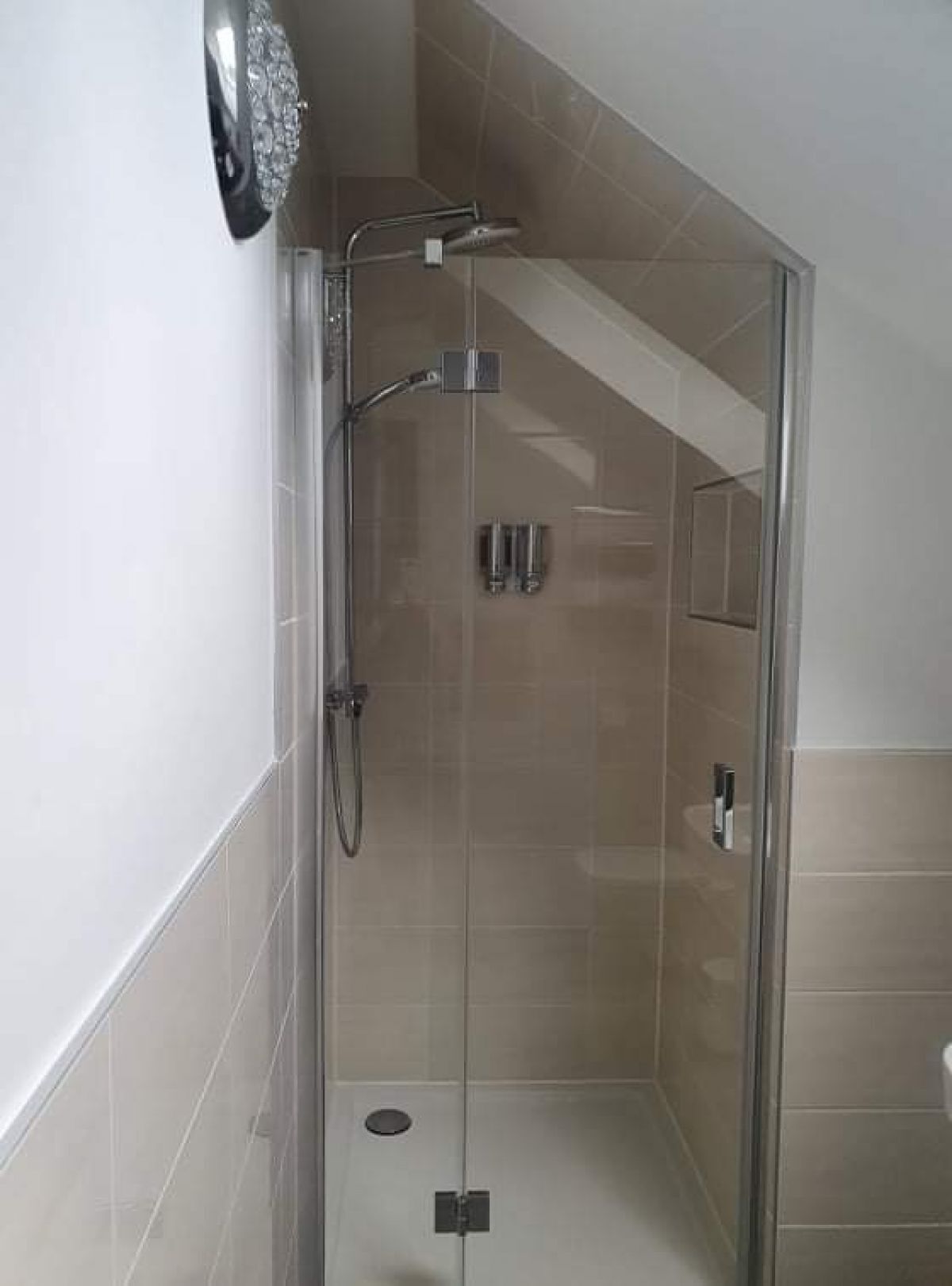 A glass-enclosed shower with a handheld showerhead and a wall-mounted faucet.