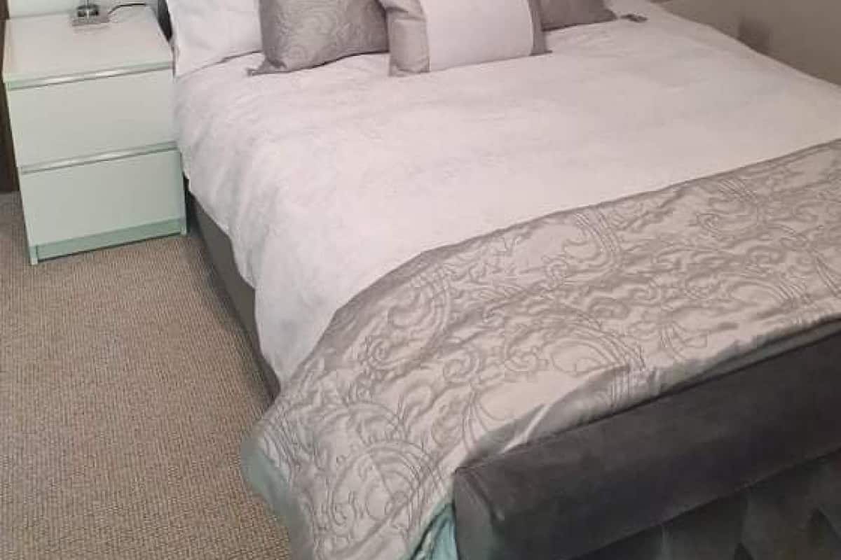 A bedroom with a tufted headboard, a bed with multiple pillows, two bedside lamps, and a nightstand with a lamp.
