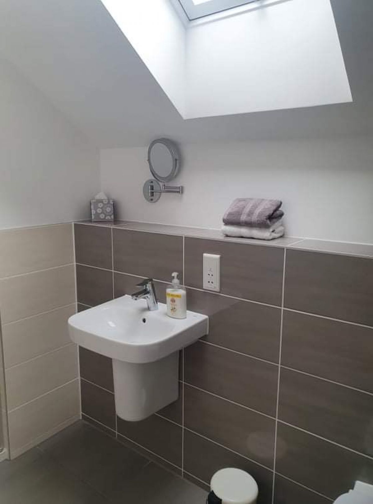 Un bagno moderno con una finestra a lucernario, un lavandino, un water e un porta asciugamani.