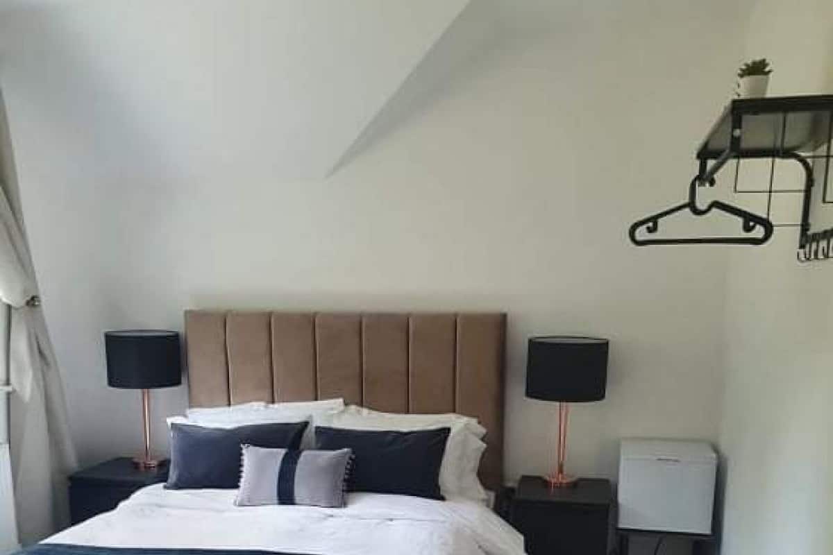 A bedroom with a large bed, two bedside tables, a hanging light fixture, and a wall-mounted coat rack.