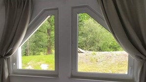 Un dormitorio con una cama, dos ventanas con cortinas, un radiador y vistas a zonas verdes.