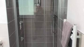 Cabina de ducha con paredes de vidrio, un cabezal de ducha manual y un grifo empotrado.