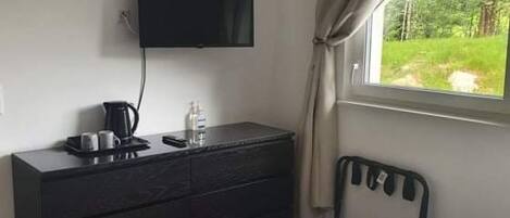 A bedroom with a bed, a dresser, a television mounted on the wall, and a window with curtains.