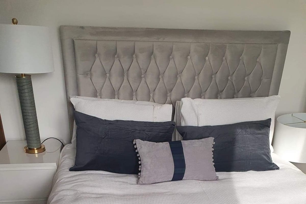 A neatly made bed with a tufted headboard, a white and dark blue bedspread, and two bedside lamps on white nightstands.