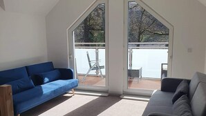 Amplia sala de estar con un sofá azul, un sofá gris y una lámpara de techo estampada. Amplias ventanas ofrecen vistas al exterior.