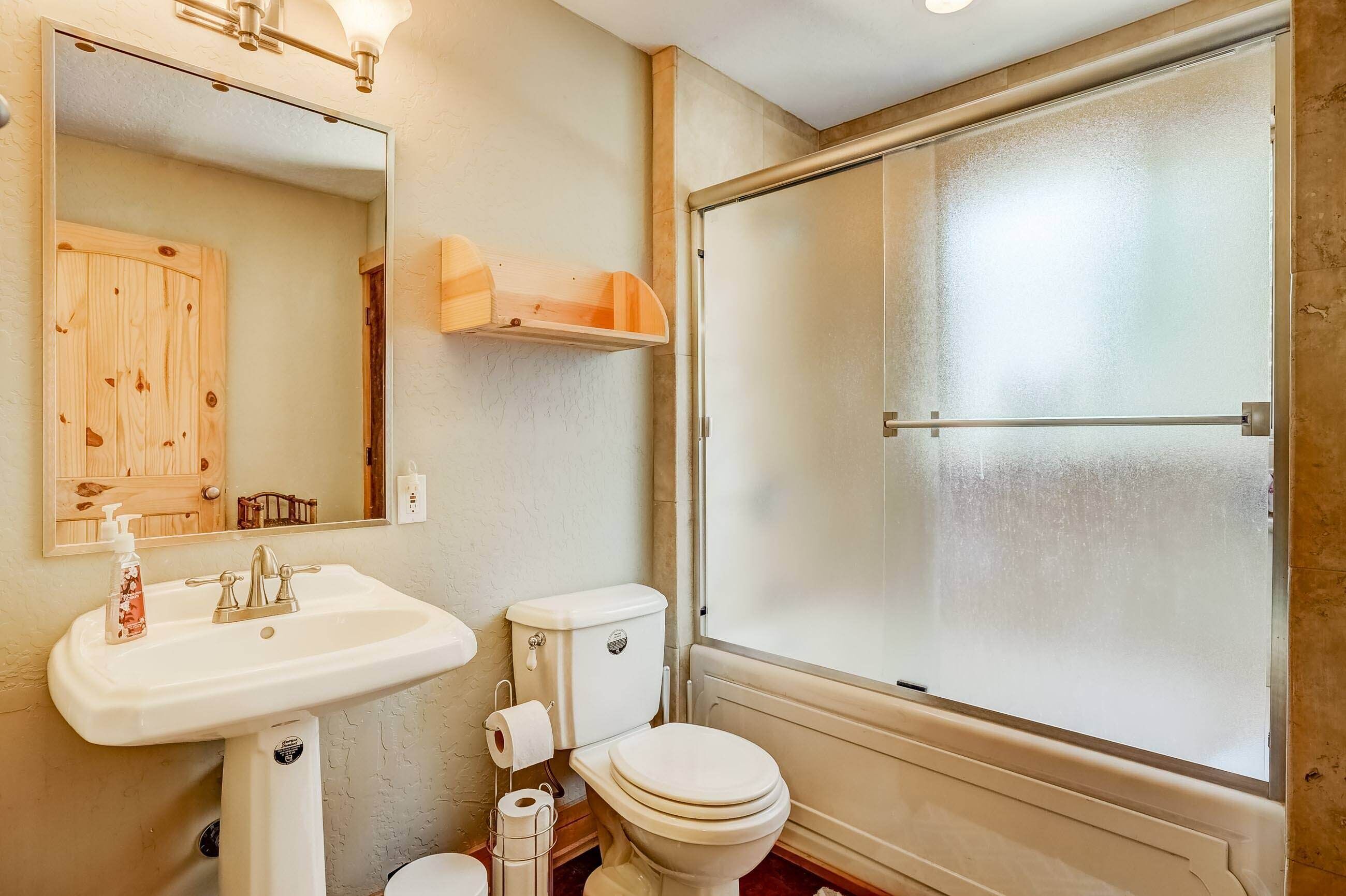 A bathroom with a wooden cabinet, a sink with a soap dispenser, a toilet, and a frosted glass shower door.