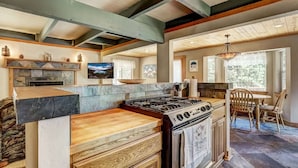 Una cocina con una estufa grande, armarios de madera y una zona de comedor con sillas y una mesa.