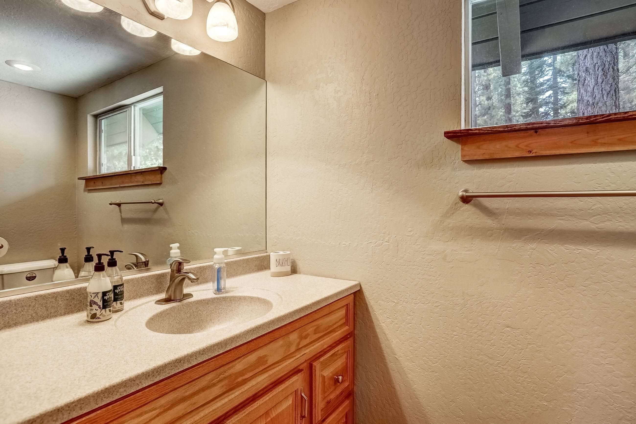 Un baño con un espejo grande, tocador de madera y ventana con vistas a árboles.