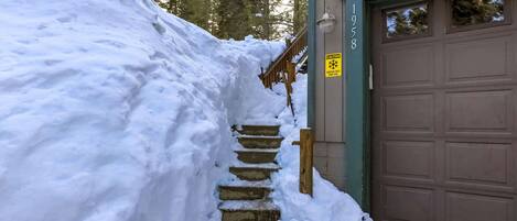 A snow-covered staircase leading to a garage with a caution sign for ice.