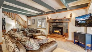 Una sala de estar acogedora con chimenea, un sofá grande, una mesa de centro de madera y una escalera.
