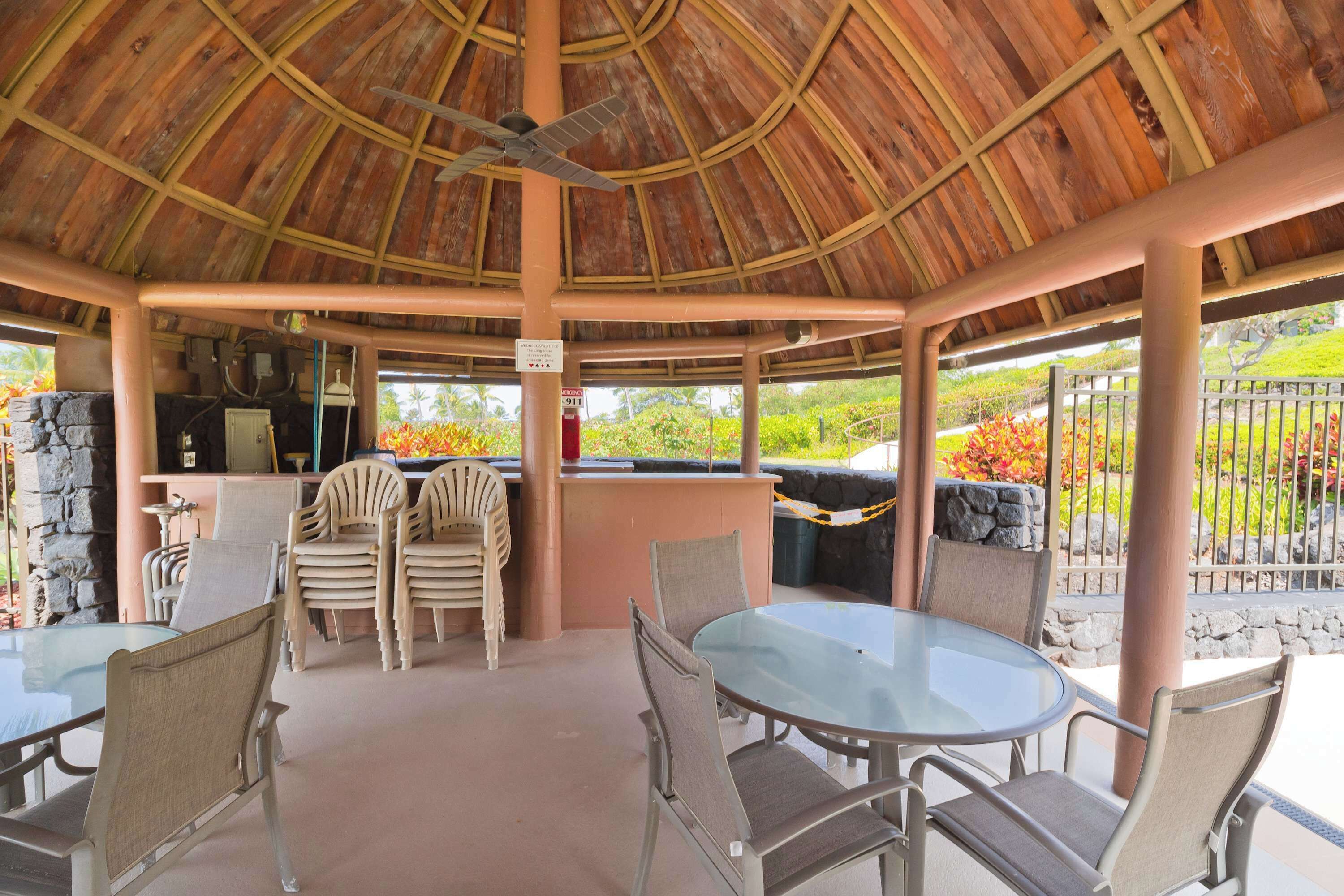 An outdoor covered patio with a thatched roof, round glass table, and cushioned chairs.