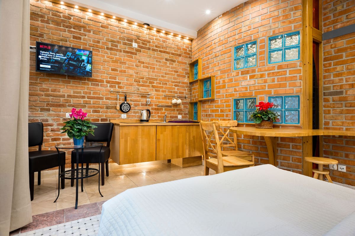 A cozy room with a brick wall, a wooden desk, two chairs, a bed, and a TV mounted on the wall.