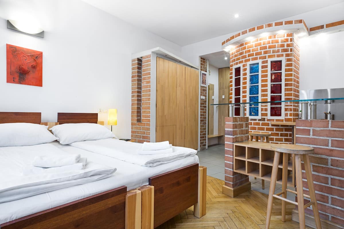 A modern hotel room with a wooden bed, a brick accent wall, a glass bar, and a wooden wardrobe.