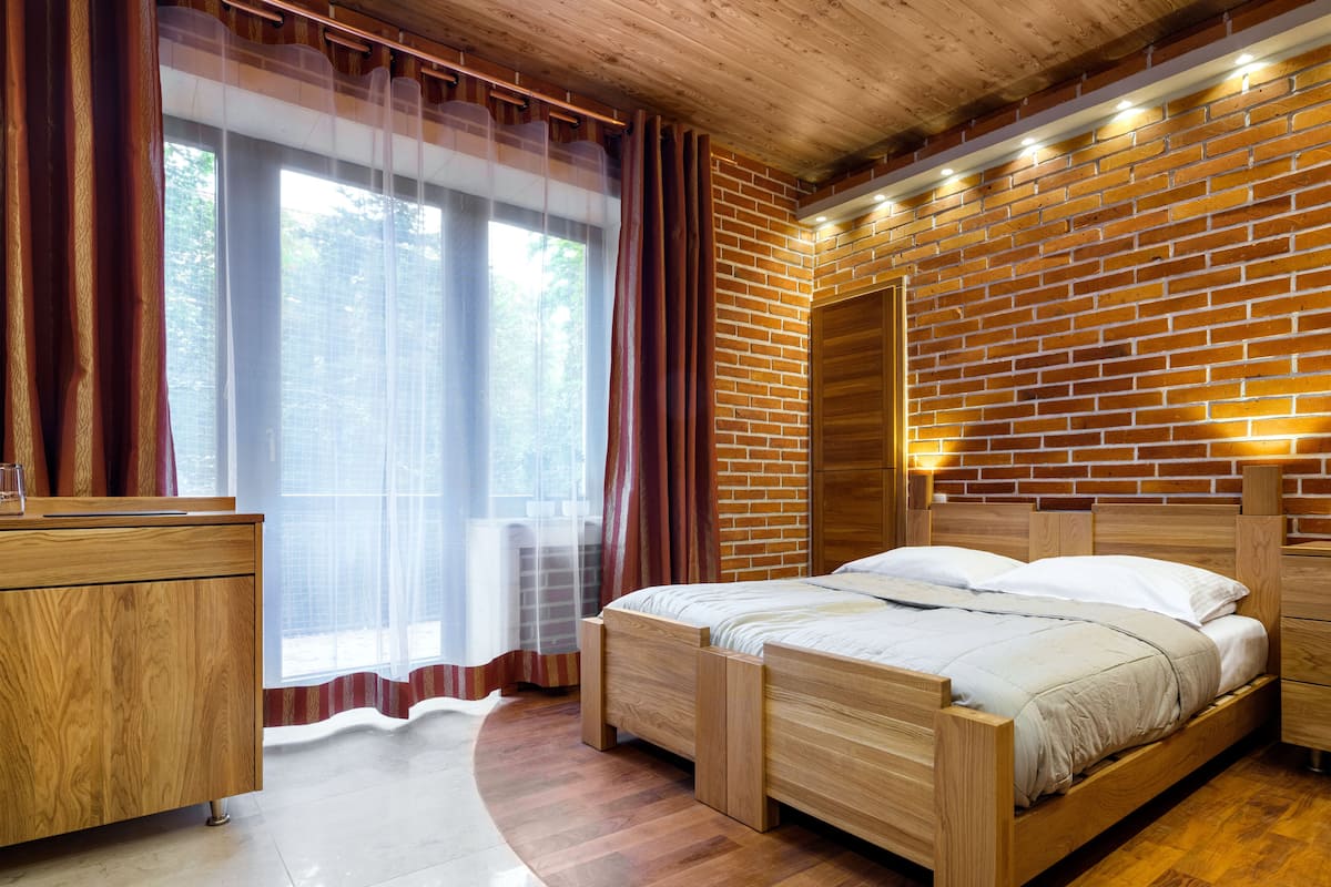A bedroom with a wooden bed, a wooden dresser, and a brick wall.