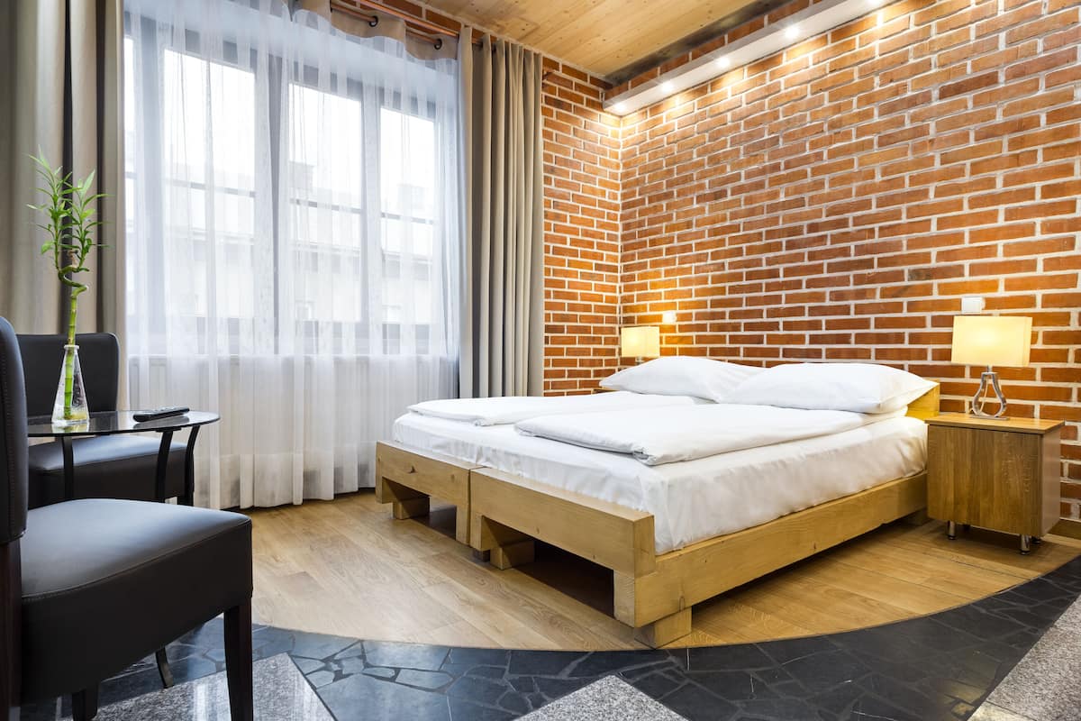 A modern hotel room with a brick wall, a wooden bed, a desk, and a chair.