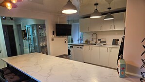 Une cuisine moderne dotée d’un plan de travail en marbre, de meubles blancs et de luminaires suspendus.