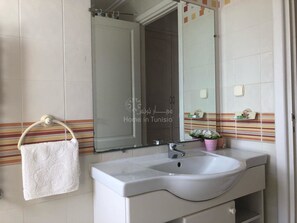 A bathroom with a white sink, a towel hanging on a rack, a mirror, and striped tiles on the wall. - Superb apartment for vaccinations (sousse)