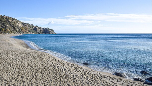 A beach with clear blue water, sandy shore, and rocky cliffs in the background. - 1 bedroom amazing apartment in Locri (Locri)