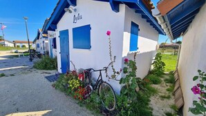 A white building with blue trim and shutters, labeled "Lulu," with a bicycle parked in front and a garden with flowers.