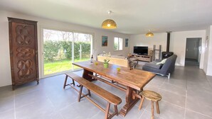 A spacious living area with a wooden dining table, benches, a sofa, and a television.