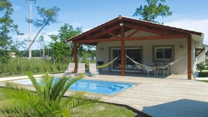 A covered outdoor area with a pool, lounge chairs, and a hammock.