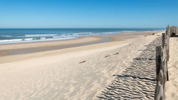 A sandy beach with a wooden fence and the ocean in the background.