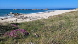 A beach with clear skies, rocky outcrops, and grassy areas with purple flowers. - Holiday Home in Cléder near Les Amiets Beach (Cléder)