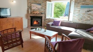 A cozy living room with a fireplace, wooden furniture, and a television. - Holiday Home in Cléder near Les Amiets Beach (Cléder)