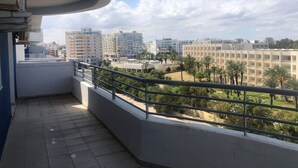 Un balcon offrant une vue sur le paysage urbain, avec des gratte-ciel et un espace aménagé avec des palmiers.