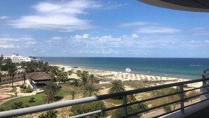 A beach view from a balcony with a clear sky, palm trees, and a beach with umbrellas. - Great waterfront apartment (Sousse)
