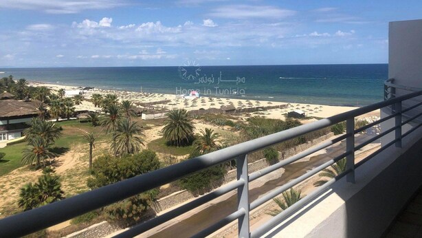 A balcony with a view of a beach, palm trees, and a clear sky. - Great waterfront apartment (Sousse)