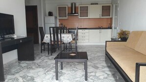 Un salon avec un canapé, un téléviseur, une table à manger avec des chaises, et une cuisine en arrière-plan.