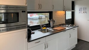 Eine moderne Küche mit integriertem Mikrowellenherd, Spülbecken aus Edelstahl und einem Fenster mit Blick auf einen Kanal.