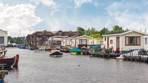 Eine Reihe von Mobilheimen an einem ruhigen Gewässer, in der Nähe liegen Boote im Hafen.