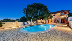 A swimming pool with lounge chairs, a stone patio, and a stone house with a tiled roof. - Nice home in Stankovci (Stankovci)