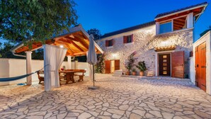 A stone-floored courtyard with a wooden pergola, a table, and chairs. - Nice home in Stankovci (Stankovci)