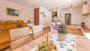 A modern living room with a sofa, wooden chairs, a dining table with a floral tablecloth, and a kitchen in the background. - Nice home in Stankovci (Stankovci)