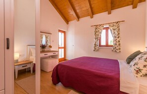 A bedroom with a wooden ceiling, a bed with a red bedspread, a nightstand with a lamp, a dresser, and a window with floral curtains. - Nice home in Stankovci (Stankovci)
