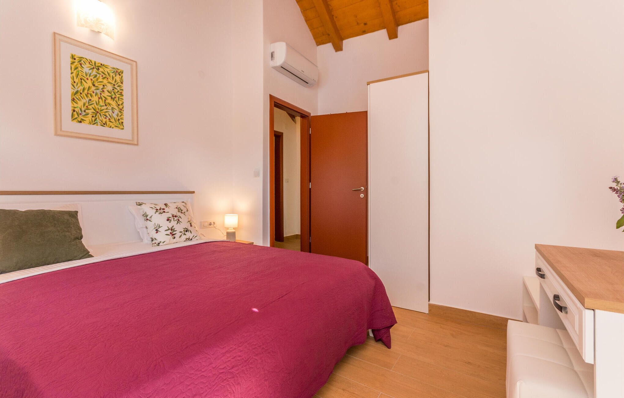Ein Schlafzimmer mit einem Bett, einem Nachttisch, einer Wand-Klimaanlage, einer Tür und einem kleinen Tisch mit Schubladen.