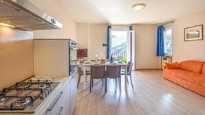 Eine kompakte Küche mit Herd, Esstisch und Stühlen. Durch eine offene Tür ist ein Balkon mit Blick auf Grünflächen zu sehen.