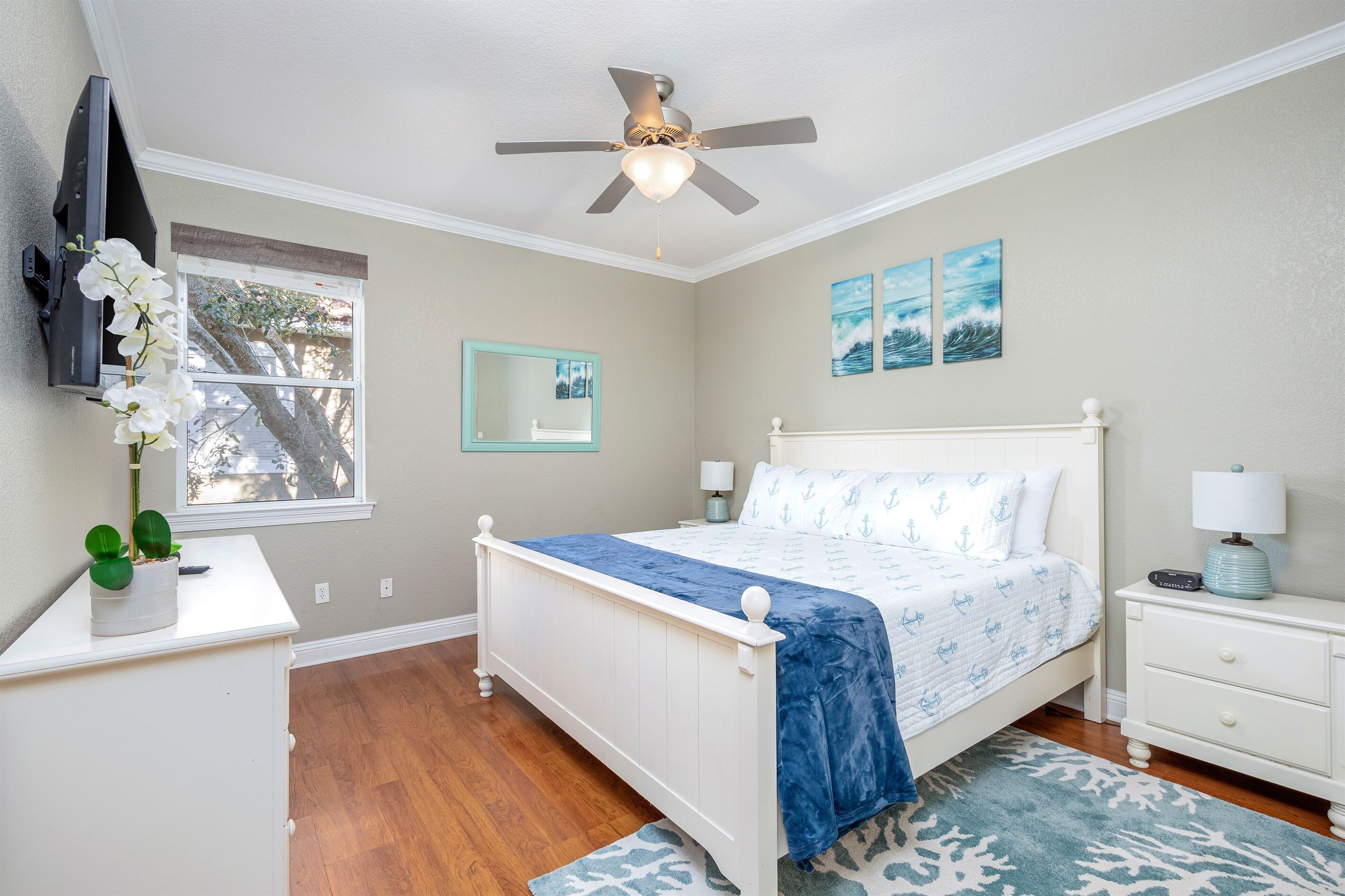 Une chambre à coucher comprenant un lit, une table de chevet, une commode, un ventilateur de plafond, une fenêtre et des œuvres d’art murales.