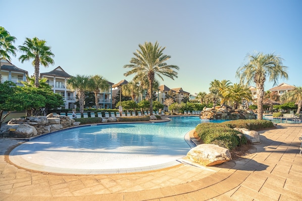 A resort pool area with a circular pool, palm trees, and resort buildings in the background.
