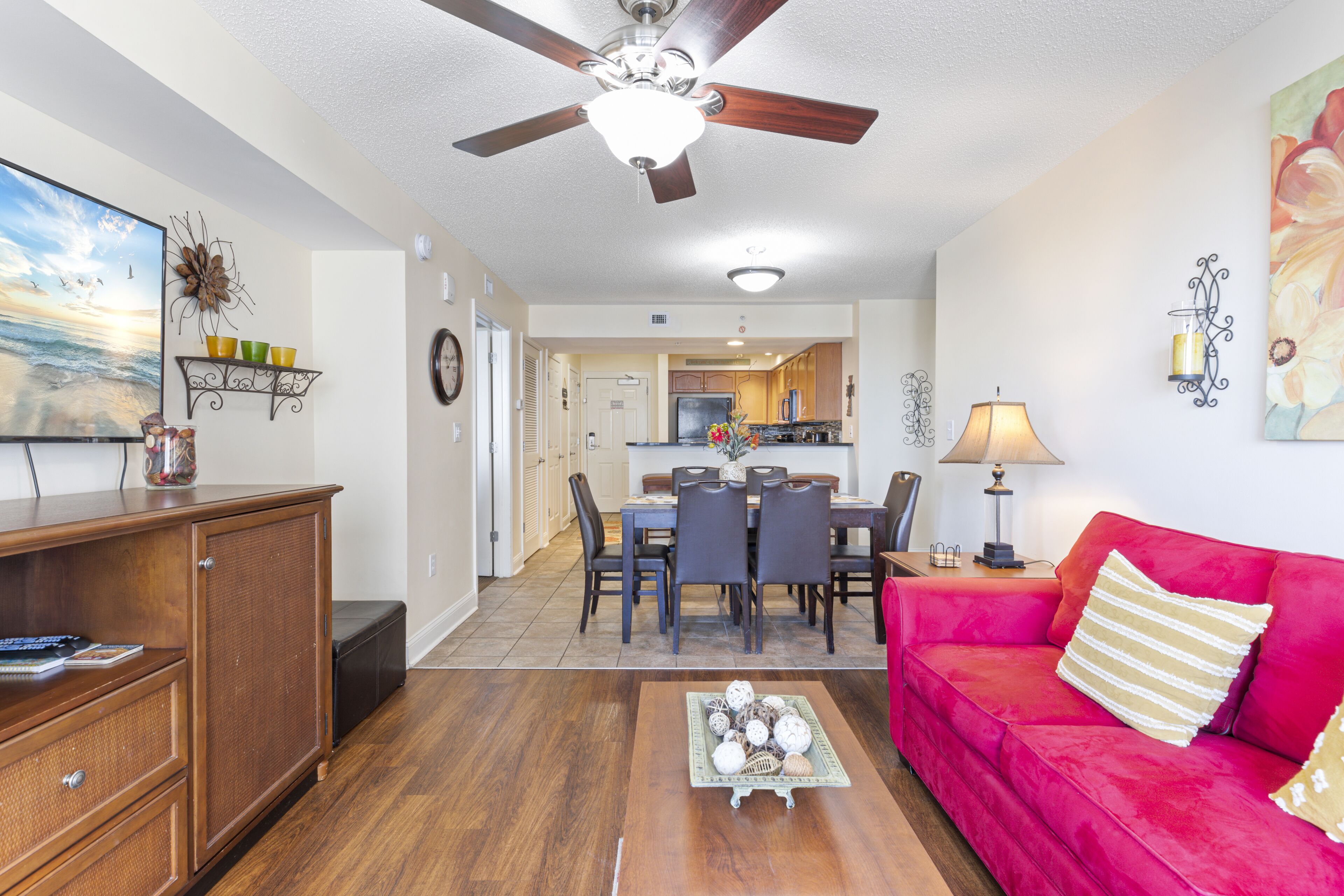 A living room with a red sofa, wooden cabinet, dining area, and kitchen in the background.